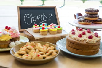 Close-up of various sweet foods on table with open signboard in cafeteria