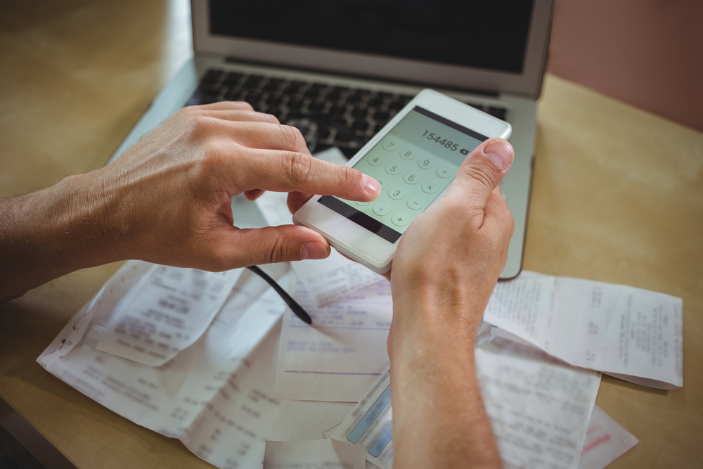 Mid section of man calculating bills on mobile phone