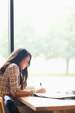 Portrait of a serious young student writing an essay in a library